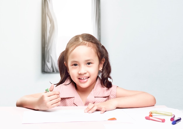 Bambina asiatica con un disegno a pastello sulla carta sul tavolo. Ritorno al concetto di scuola