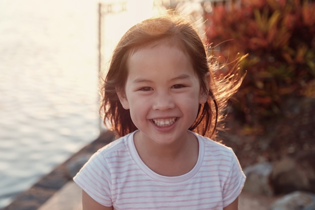 Bambina asiatica felice che ride con il fondo del chiarore del sole dal lago