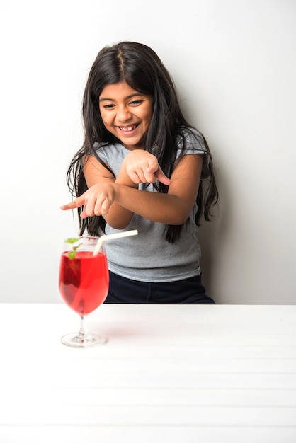 Bambina asiatica indiana carina in posa con bevanda fredda o succo di frutta fresco a tavola su sfondo bianco