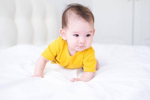bambina asiatica sana 5 mesi in tuta gialla sul letto su biancheria da letto bianca