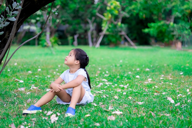 Bambina asiatica sveglia che si siede nel parco e alzò lo sguardo