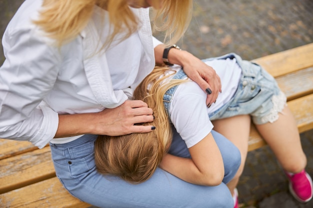 Bambina assonnata sulle gambe della donna mentre trascorre del tempo all'aria aperta in una panca di legno