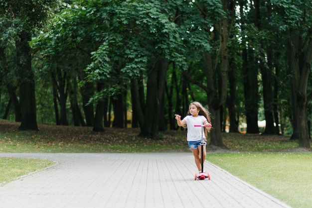 Bambina attiva che guida scooter su strada nel parco all'aperto il giorno d'estate