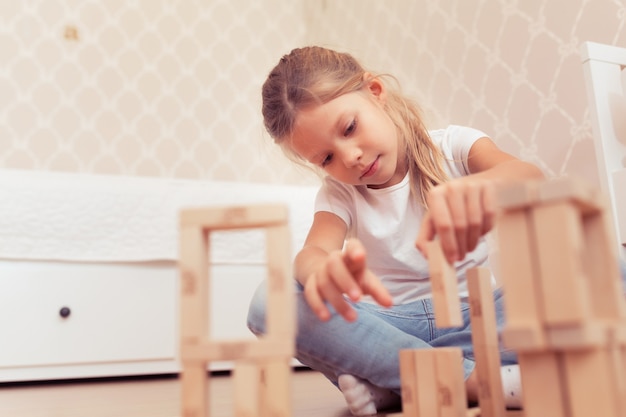 Bambina bambina che gioca con blocchi di legno la torre instabile