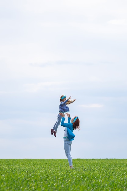 Bambina bambina e madre donna corrono e saltano, erba verde nel campo, tempo primaverile soleggiato, sorriso e gioia del bambino, cielo blu con nuvole