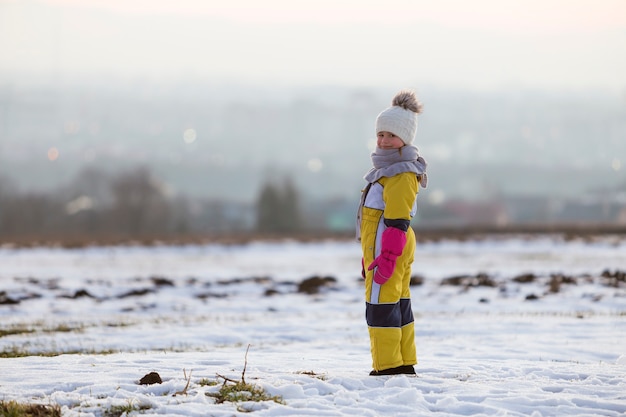 Bambina bambino in piedi all'aperto da solo sul campo invernale di neve.