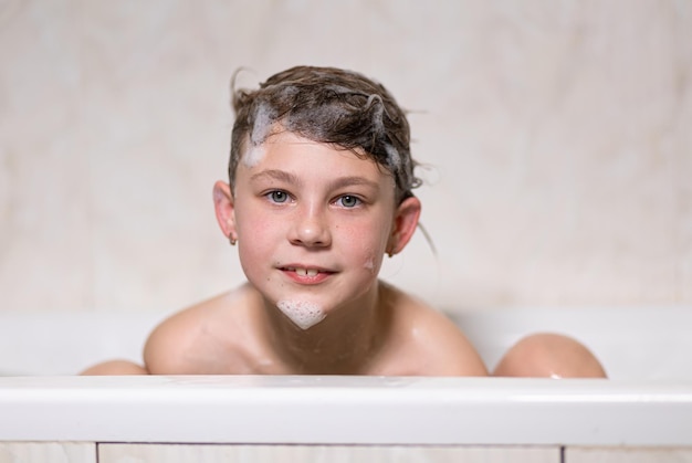 Bambina bella bambina si bagna seduto in un bagno bianco con schiuma di sapone shampoo e si lava la testa con i capelli Fotografia di modello