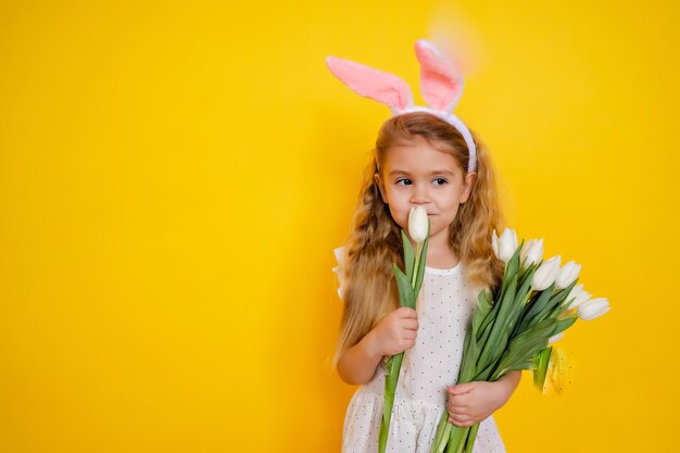 bambina bionda con orecchie da coniglio il giorno di Pasqua che tiene fiori tulipani bianchi nelle sue mani