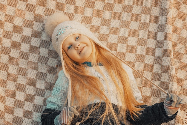 Bambina bionda con un cappello di lana in un plaid nel parco