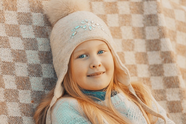 Bambina bionda con un cappello di lana in un plaid nel parco