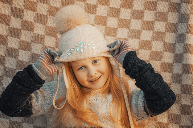 Bambina bionda con un cappello di lana in un plaid nel parco