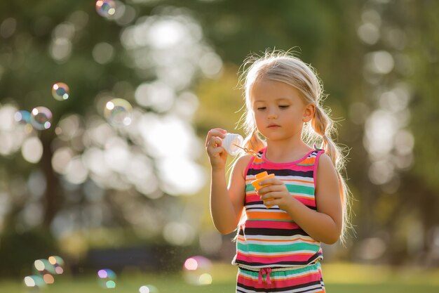 bambina bionda gonfia le bolle di sapone in estate in una passeggiata