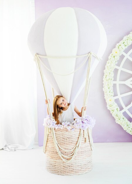 Bambina bionda graziosa in un vestito bianco che sta nella bella mongolfiera decorativa