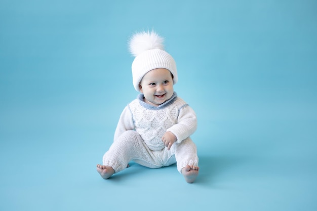 Bambina bionda in un cappello lavorato a maglia invernale bianco e maglione lavorato a maglia su sfondo blu isolare lo spazio per il testo bambino bambino in abiti invernali