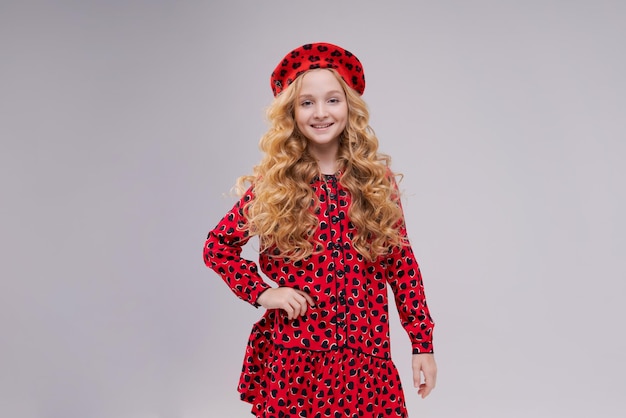 Bambina bionda pensierosa con capelli ricci lunghi ritratto closeup ragazza sorridente carina in un berretto rosso un