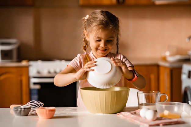 Bambina bionda sorridente sveglia che cucina pasta in cucina a casa