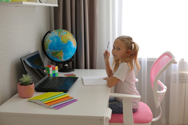 bambina bionda studentessa a casa insegna lezioni online quaderni di istruzione globo laptop