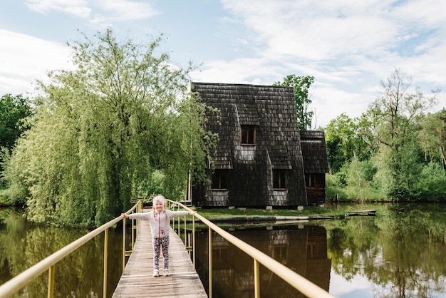 Bambina cammina su un ponte di legno che attraversa un fiume o un lago Vecchia casa di legno sull'isola