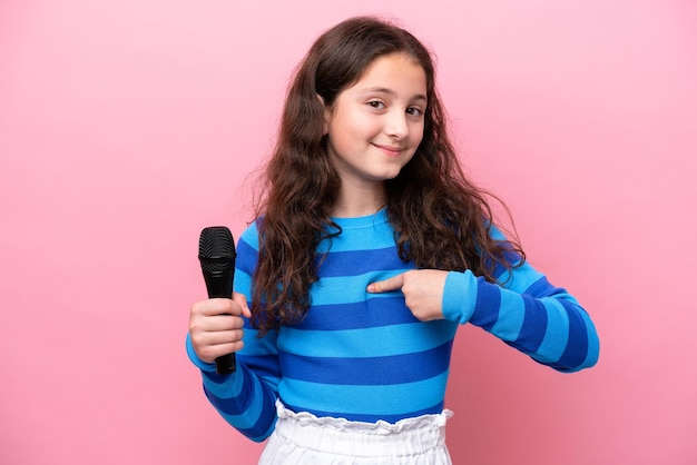 Bambina cantante che raccoglie un microfono isolato su sfondo rosa con espressione facciale a sorpresa