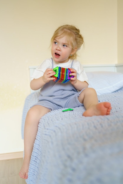 Bambina carina che guarda lontano mentre gioca con il giocattolo di costruzione magnetico nella stanza dei bambini