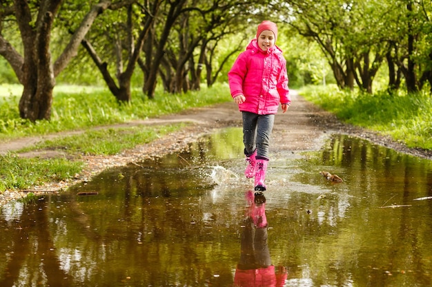 bambina carina che indossa stivali da pioggia che salta in una pozzanghera