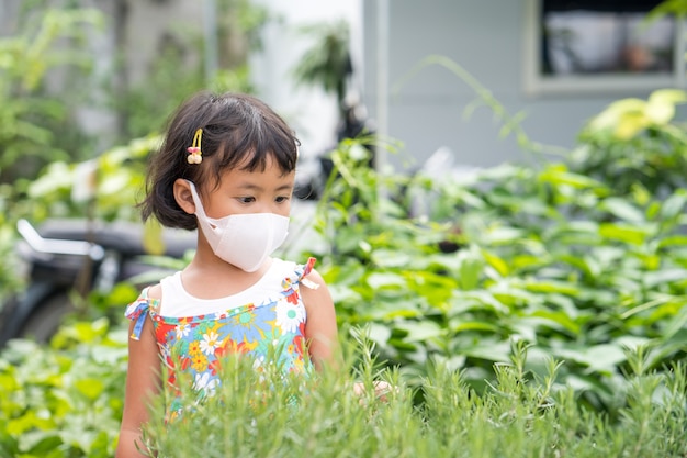 Bambina carina che indossa una maschera protettiva che guarda la pianta di rosmarino