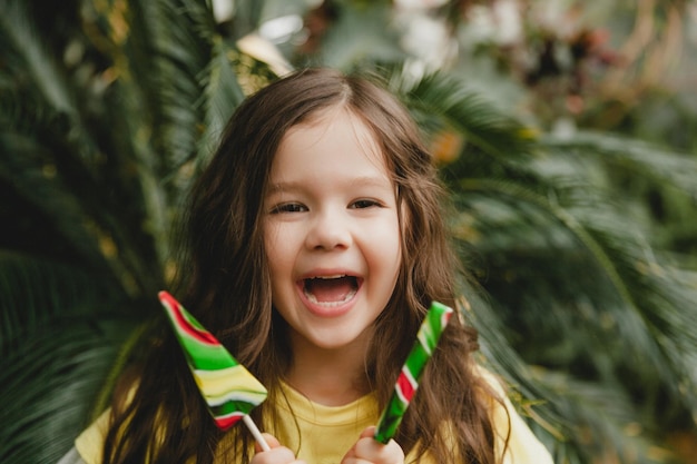 Bambina carina che mangia un lecca-lecca a forma di anguria Bambino con lecca-lecca nel giardino botanico