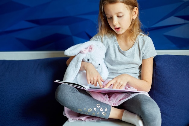 Bambina carina che mangia un libro con un peluche a forma di coniglietto di peluche