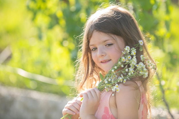 Bambina carina che raccoglie fiori nel giardino estivo in fiore Volto di bambino di primavera Bambina felice con fiori sull'erba in un'estate Bambina carina sul prato nel cortile di casa