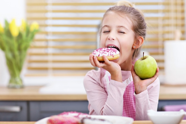 Bambina carina che sceglie tra spuntino sano e malsano in cucina