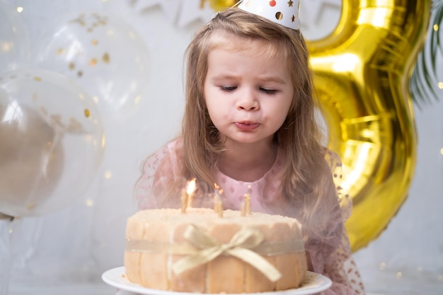 Bambina carina che soffia candele sulla torta di compleanno e festeggia il compleanno