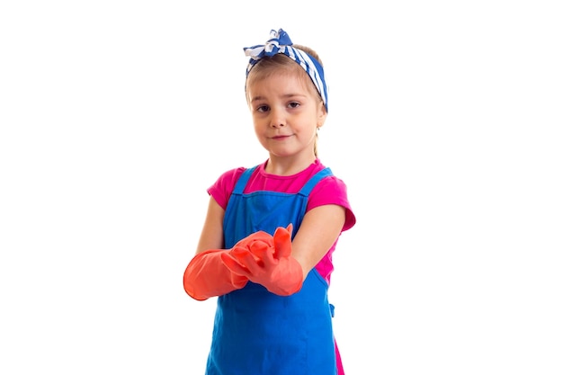 Bambina carina con coda di cavallo che indossa in camicia rosa e grembiule blu con guanti rossi in studio