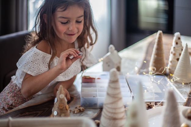 Bambina carina con i capelli ricci che fa mestieri e decora il cono dell'albero di Natale con i bottoni