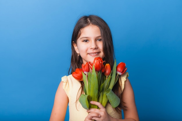 Bambina carina con in mano un mazzo di tulipani su sfondo blu Buona festa della donna Posto per il testo Emozioni vivide 8 marzo