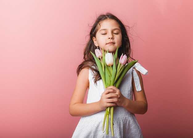 Bambina carina con in mano un mazzo di tulipani su sfondo rosa Buona festa della donna Posto per il testo Emozioni vivide 8 marzo