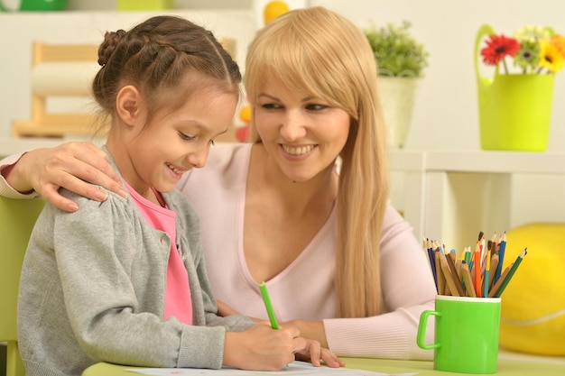 Bambina carina con la madre che disegna a casa