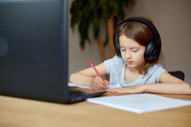 Bambina carina con le cuffie che usa il laptop per studiare a casa