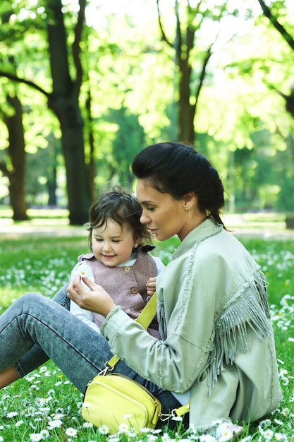 Bambina carina con sua madre seduta su un prato con fiori di camomilla in un parco cittadino