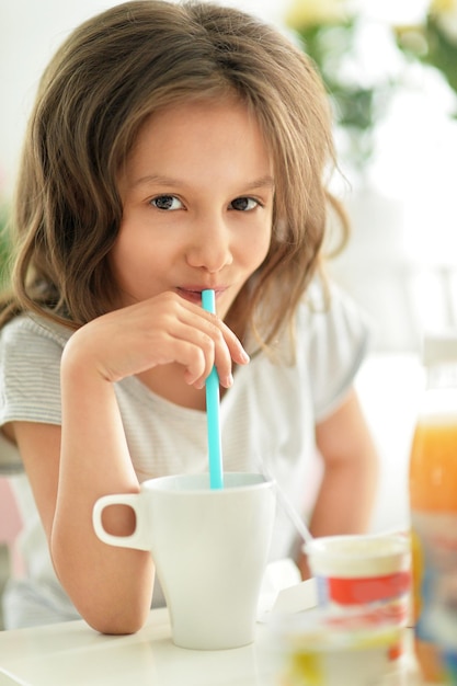 Bambina carina con una tazza che beve sul tavolo