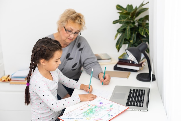 Bambina carina e felice che utilizza il computer portatile con sua nonna, studiando attraverso il sistema di e-learning online.