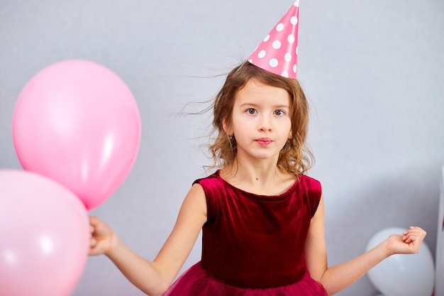 Bambina carina e gioiosa in abito rosa e cappello gioca con i palloncini alla festa di compleanno a casa