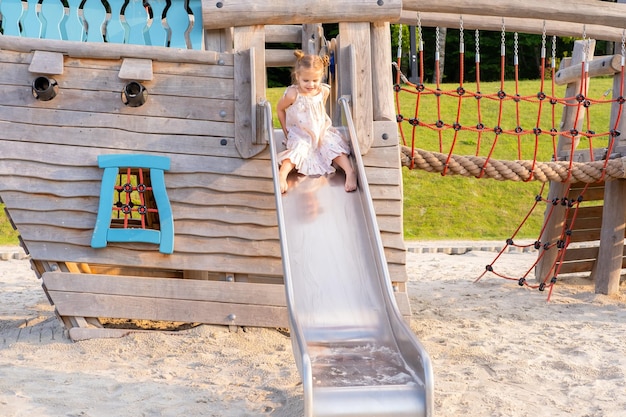 bambina carina in abito che gioca nel parco giochi per bambini in una giornata estiva