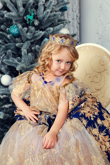 Bambina carina in abito da principessa vicino all'albero di Capodanno, bellissime decorazioni natalizie