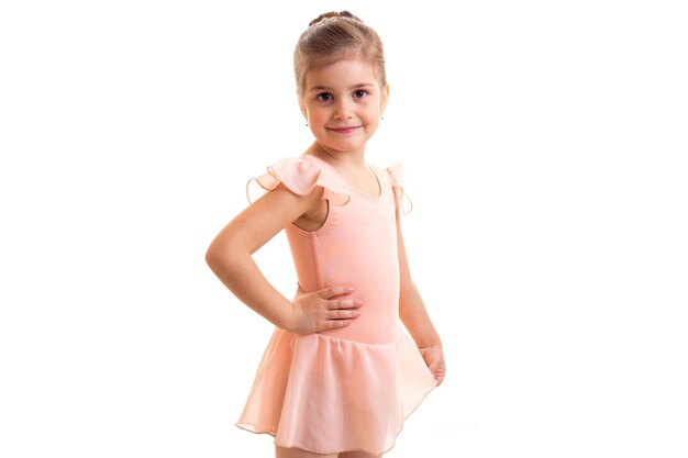 Bambina carina in abito rosa con fascio che balla su sfondo bianco in studio