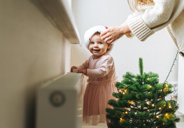 Bambina carina in abito rosa e cappello da Babbo Natale con sua madre giovane donna in camera a casa Natale a casa felice anno nuovo