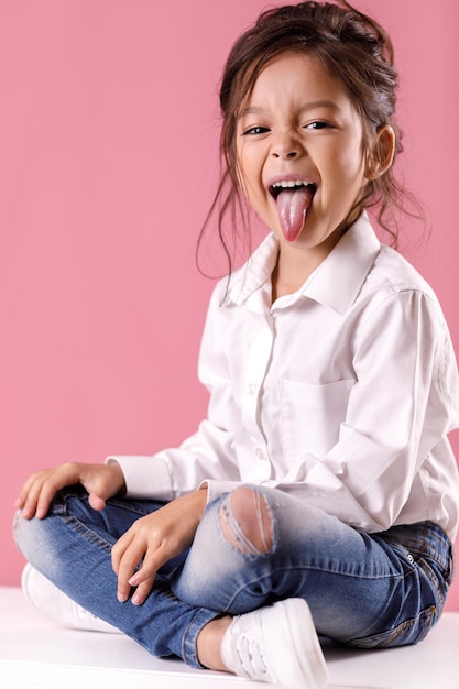 Bambina carina in camicia bianca con l'acconciatura che mostra la lingua