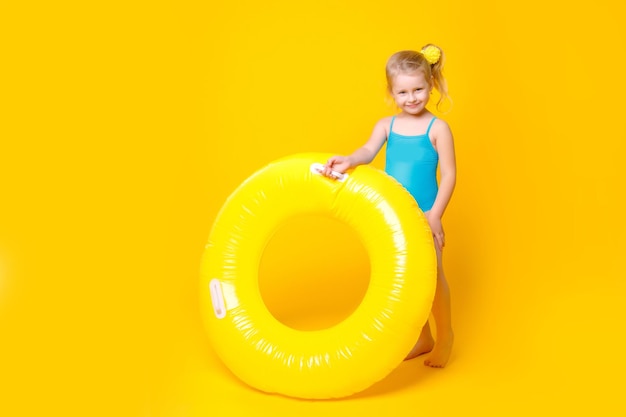 bambina carina in costume da bagno e occhiali da sole con un cerchio su sfondo giallo