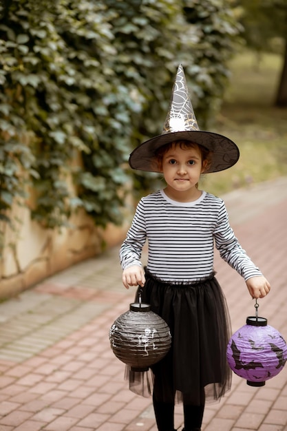 Bambina carina in costume da strega che tiene lanterne di carta Bambino che si diverte durante le vacanze di Halloween