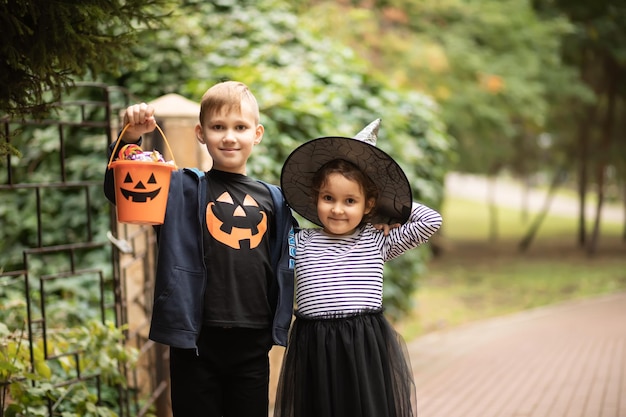 Bambina carina in costume da strega e ragazzo che tiene secchio di zucca jack-o-lantern con caramelle e dolci. Dolcetto o scherzetto per bambini durante le vacanze di Halloween.