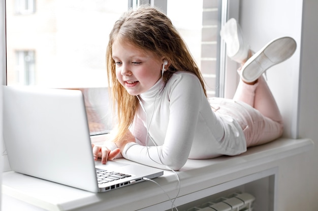 Bambina carina in cuffia che usa il laptop a casa per l'istruzione online e lo studio a casa